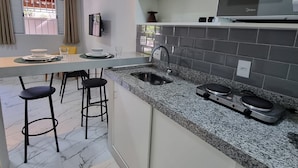 Una cocina moderna con encimera de granito, lavaplatos de acero inoxidable y horno empotrado. Hay dos taburetes de bar y una mesa de comedor con sillas.