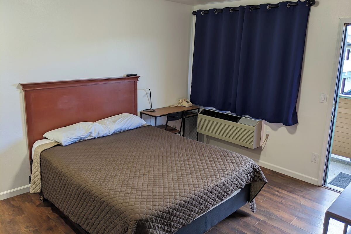 A bedroom with a bed, a desk, a chair, a heater, and a window with curtains.