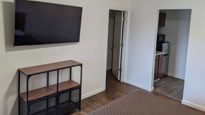 Una habitación con una televisión de pantalla plana montada en la pared, una mesita de madera y una puerta que da a una zona de cocina.