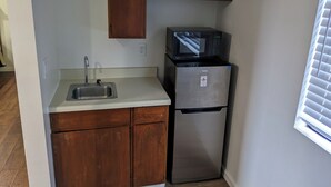 Una cocina compacta con refrigerador de acero inoxidable, microondas y armarios de madera.