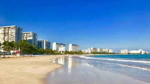 A beach with a sandy shore and a row of high-rise buildings in the background. - Sleep with the sound of waves! (Carolina)