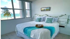 A bedroom with a bed, a window with a view of the beach, and a framed picture on the wall. - Sleep with the sound of waves! (Carolina)