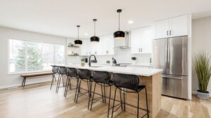 A modern kitchen with a central island, bar stools, stainless steel appliances, and pendant lighting.
