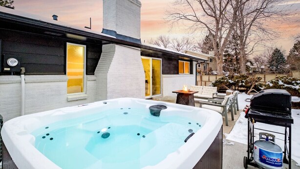 A modern house with a hot tub, outdoor seating, and a propane tank.