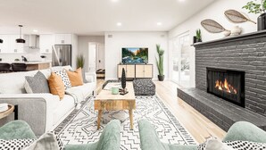 A modern living room with a fireplace, a sofa, a coffee table, and a kitchen in the background.