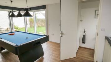 A pool table with three hanging lamps, a door leading to a balcony, and a view of a garden.