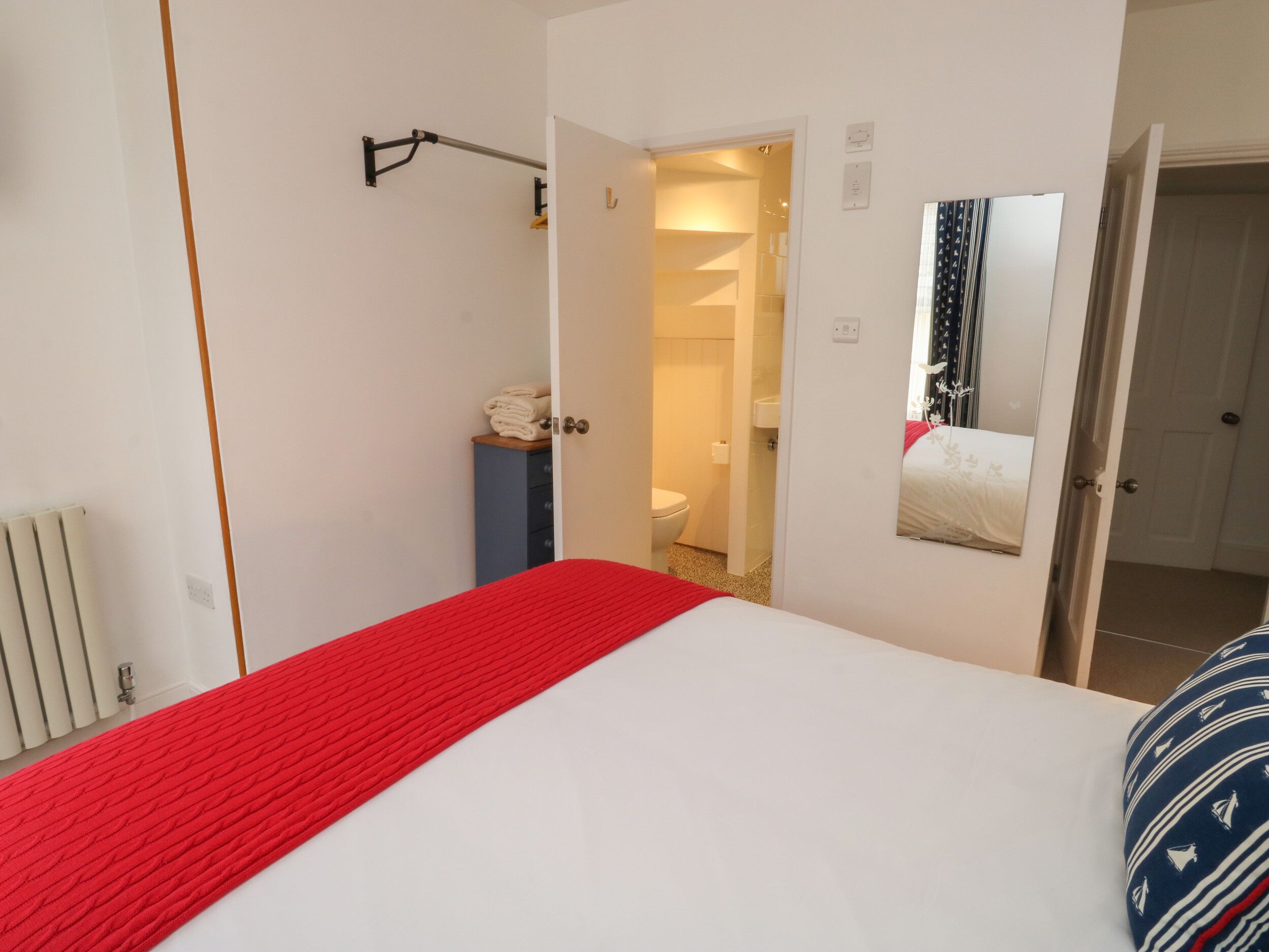 Een slaapkamer met een bed, een rode deken, een spiegel en een deur naar een badkamer.