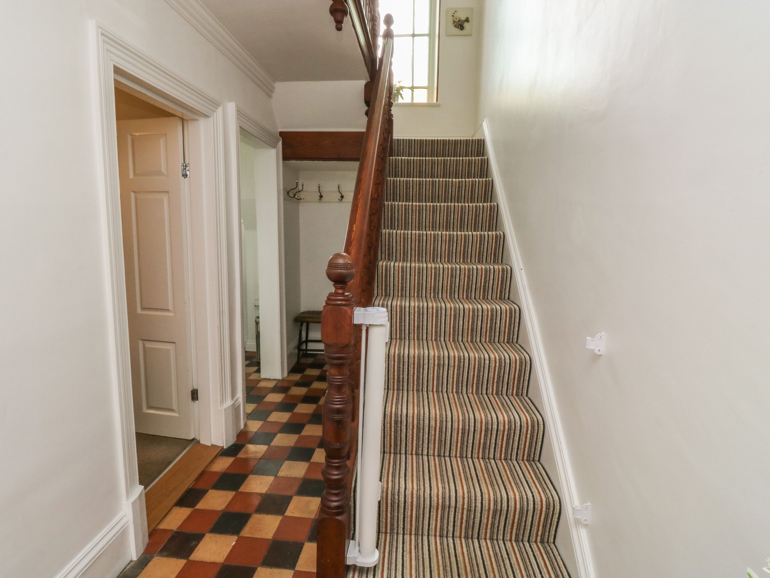 A staircase with a wooden handrail and striped carpet, leading to a room with a checkered floor and a door.