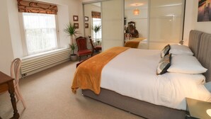 A bedroom with a large bed, a chair, a desk, a window with blinds, a potted plant, and a mirror. - Lands House (Bideford)