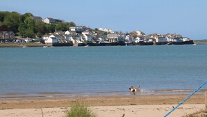 A coastal town with houses along the water, a sandy beach, and a dog running on the shore. - Lands House (Bideford)