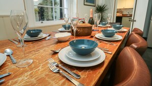 A dining table set with blue bowls, plates, and silverware, with a bottle of champagne and a vase of flowers. - Lands House (Bideford)