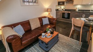 A cozy living room with a brown leather sofa, a wooden coffee table, and a dining area with a wooden chair and table. - Mulberry Tree (Bideford)