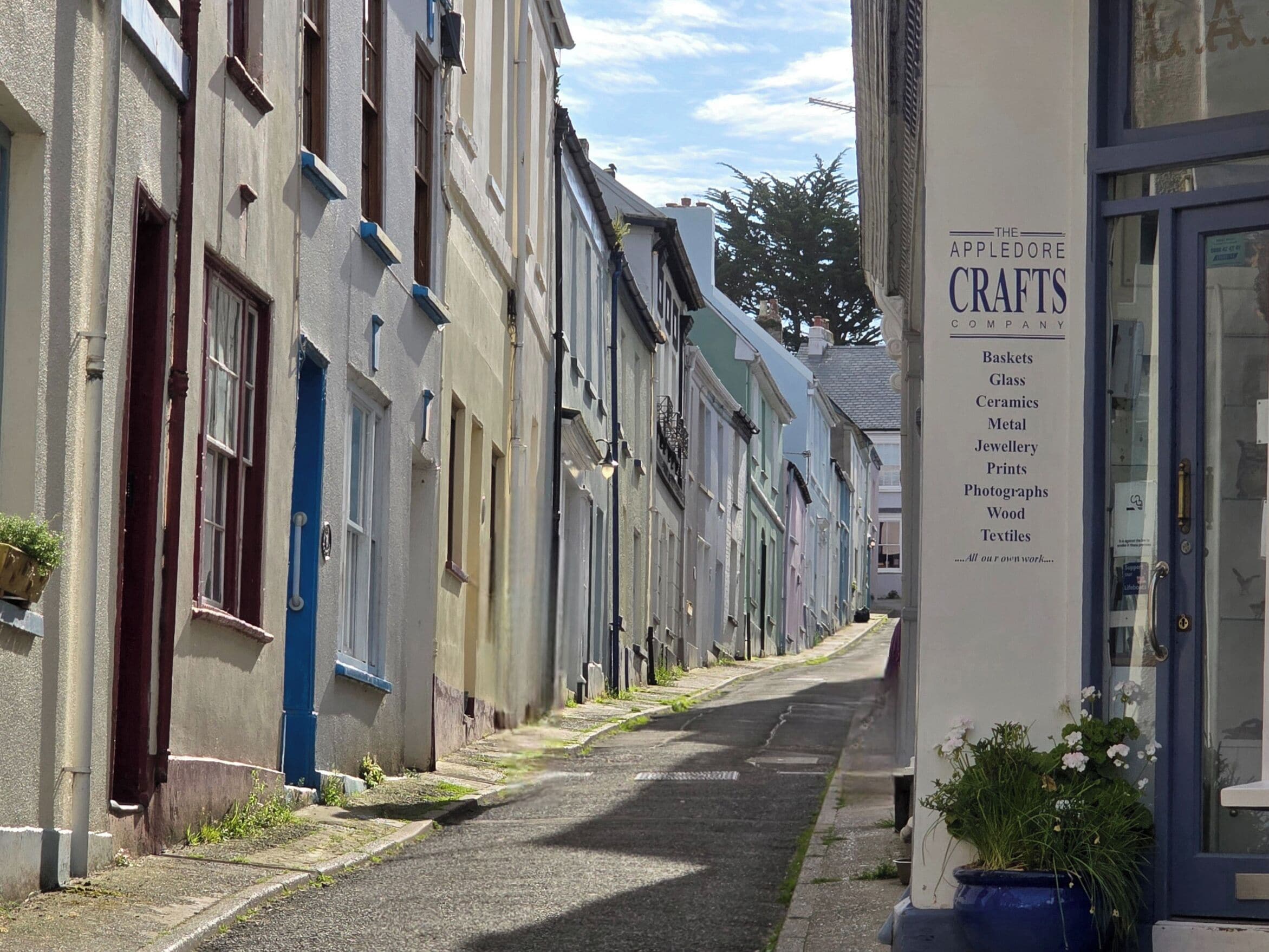 Una calle estrecha bordeada de edificios tradicionales, uno de los cuales muestra un cartel publicando diversos artículos artesanales.