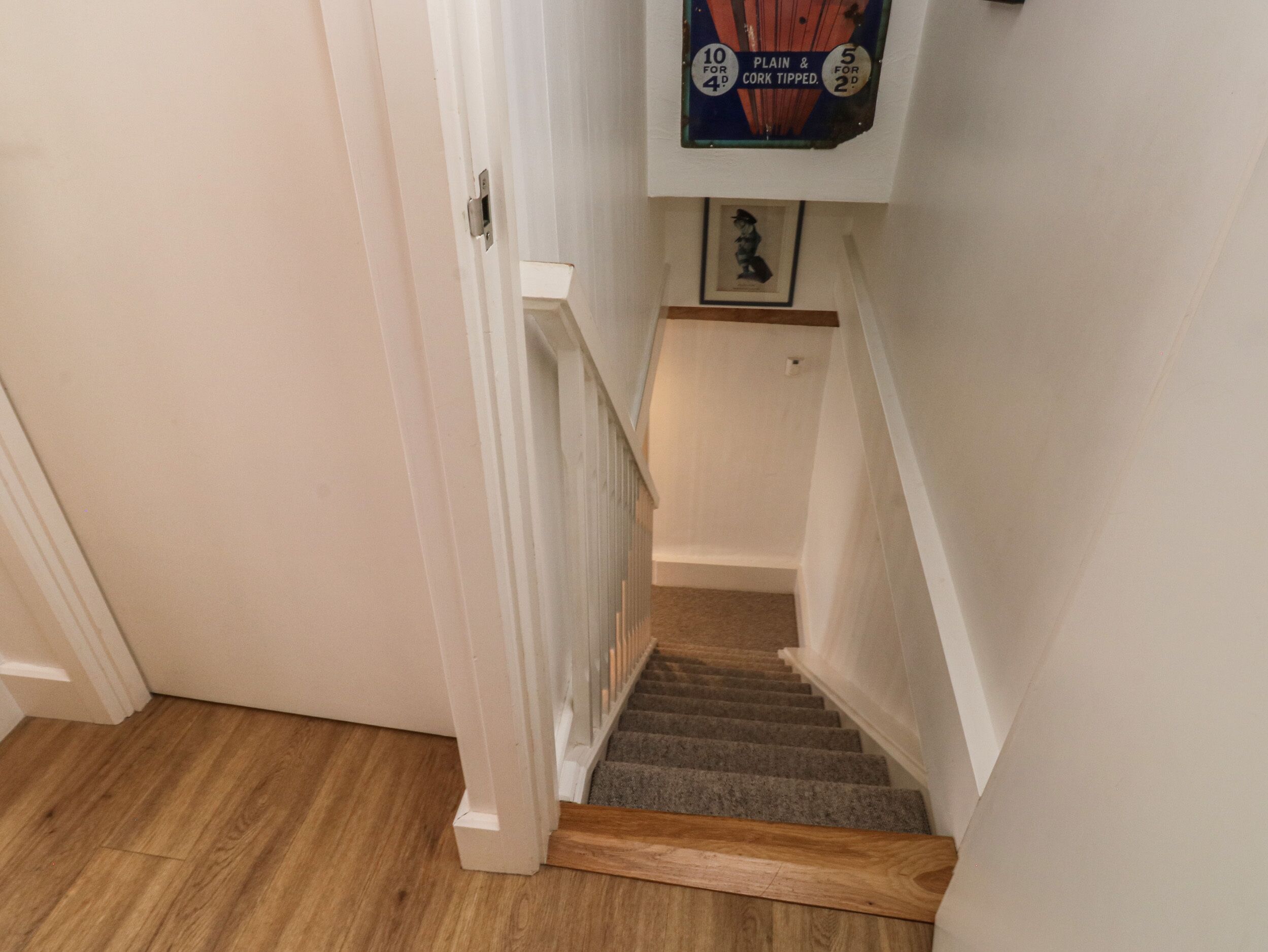 A staircase with wooden steps and white railings, leading to a landing with a framed picture.