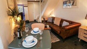 A dining area with a table set for two, a brown leather sofa, a staircase, and a framed painting on the wall. - Mulberry Tree (Bideford)