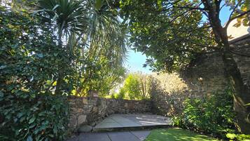 Un mur de pierres, une terrasse dallée et une zone herbeuse avec des arbres.