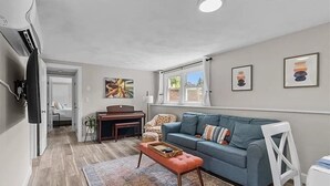 Een ruime woonkamer met een blauwe bank, een houten bijzettafeltje en een kamerbreed tapijt.