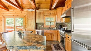 Una cocina con armarios de madera, encimera de granito, electrodomésticos de acero inoxidable y vistas al exterior.