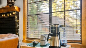 A coffee maker on a wooden table near a window with blinds, a brick fireplace, and a leather chair. - Silver Linings+Hot Tub+Pet Friendly+EV+Moonridge (Big Bear Lake)