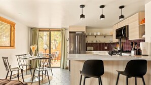 A modern kitchen with a central island, wooden cabinets, and a dining area with chairs and a table. - Silver Linings+Hot Tub+Pet Friendly+EV+Moonridge (Big Bear Lake)
