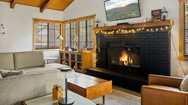 A cozy living room with a fireplace, a sofa, a coffee table, and a television mounted on the wall. - Silver Linings+Hot Tub+Pet Friendly+EV+Moonridge (Big Bear Lake)