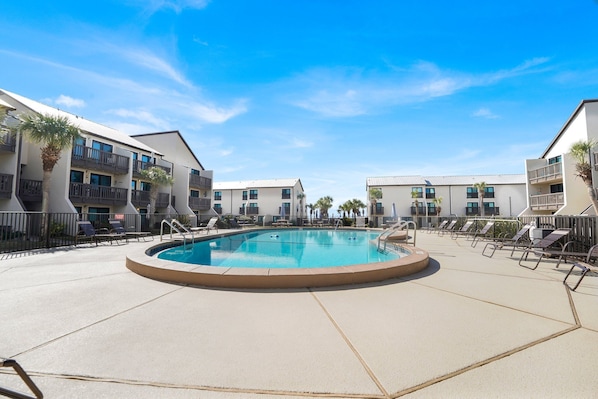 A pool area with lounge chairs and a clear blue sky.