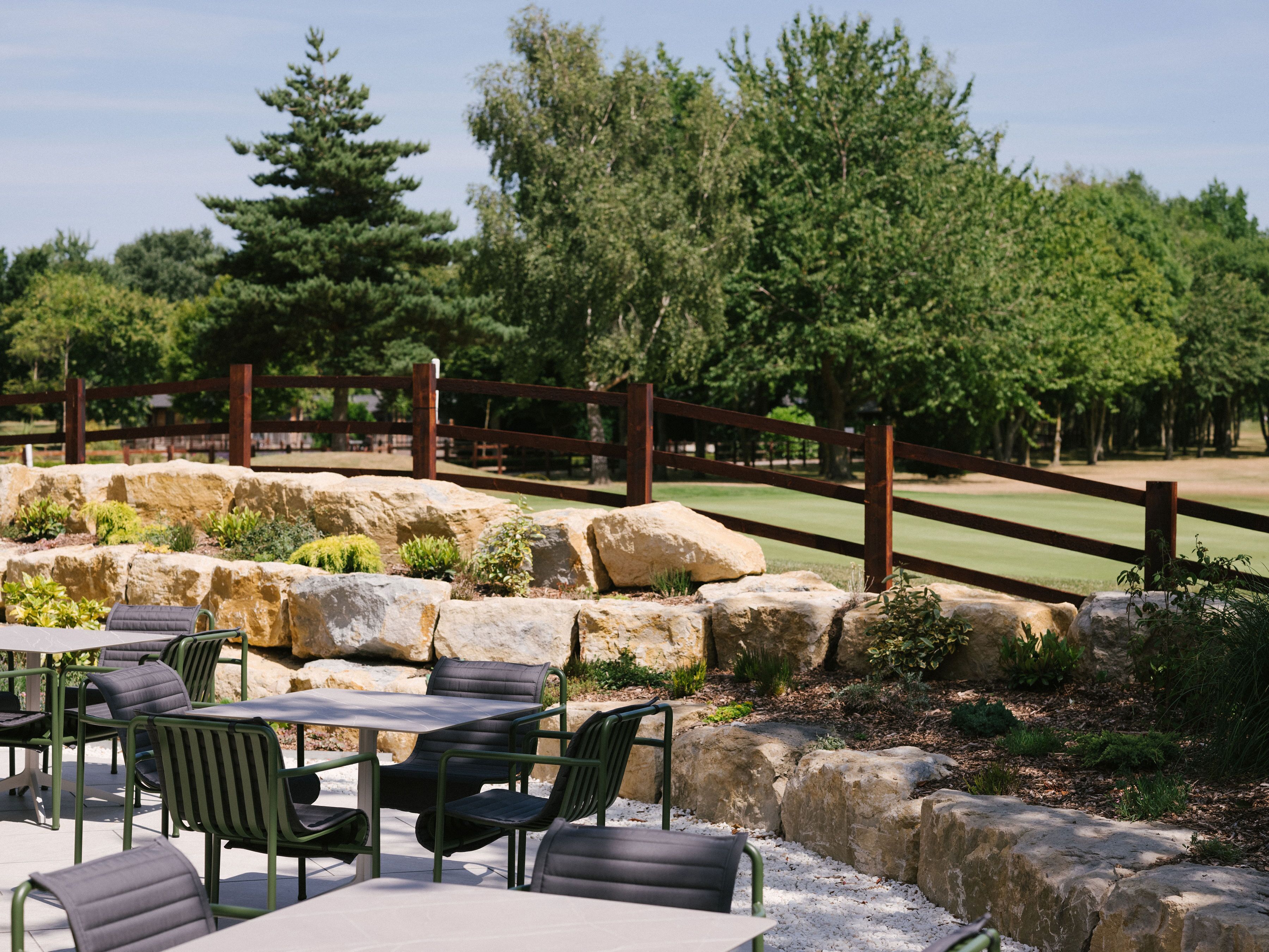 An outdoor seating area with tables and chairs, surrounded by a wooden fence and large rocks.