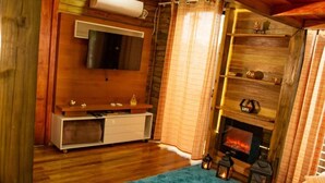 A cozy cabin interior with a fireplace, wooden shelves, a TV mounted on the wall, and a blue carpet. - Cabanas Aconchego dos Canyons (Praia Grande)