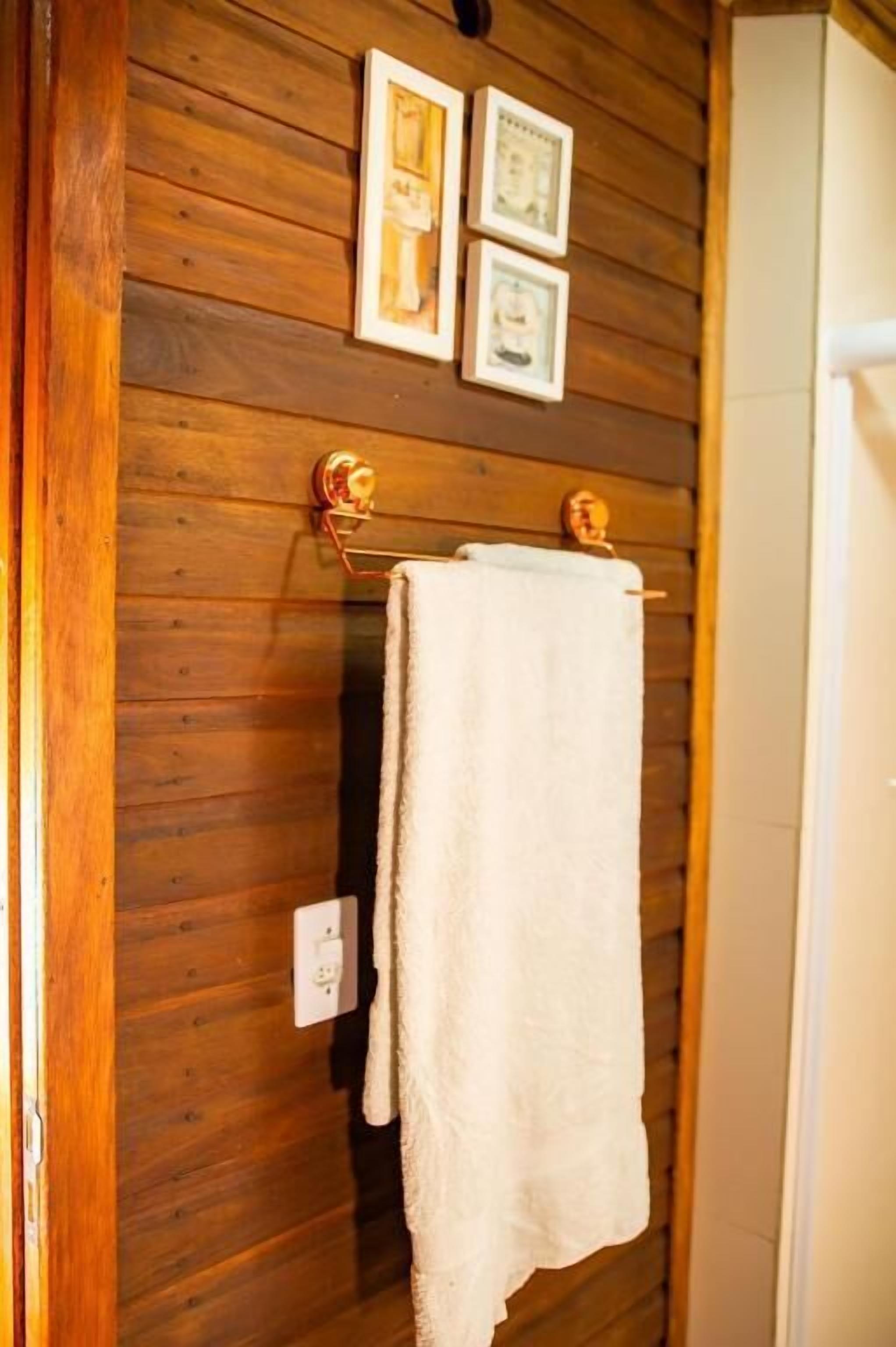 Eine Holzwand mit einem Handtuchhalter, an dem ein weißes Handtuch hängt. Darüber befinden sich drei gerahmte Bilder.