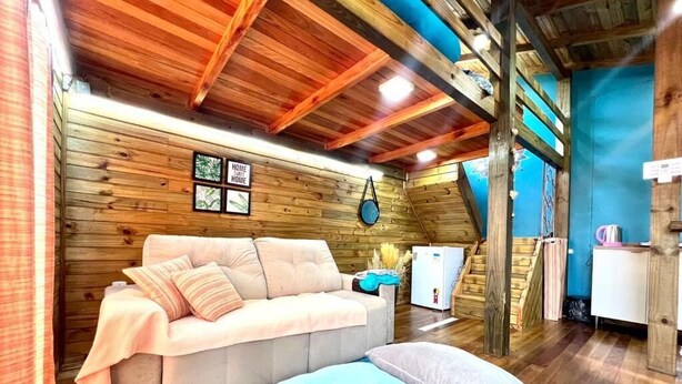A cozy log cabin interior with a sofa, pillows, a small refrigerator, and a blue rug. - Cabanas Aconchego dos Canyons (Praia Grande)