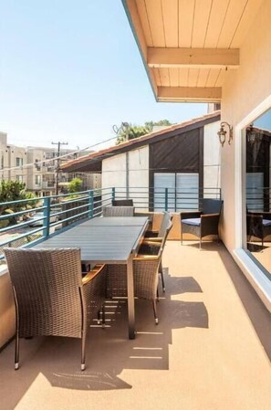A rooftop terrace with a dining table and chairs, a blue railing, and a view of neighboring buildings.
