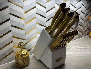 A kitchen with a white and gold patterned backsplash, a gold-colored utensil holder, and a decorative candle holder.