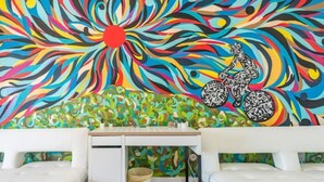 Una habitación con un escritorio blanco, dos sofás blancos y un mural abstracto y colorido en la pared.
