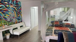 Un dormitorio con cama con dosel, un mural abstracto y lleno de color, un banco blanco y un escritorio con silla.