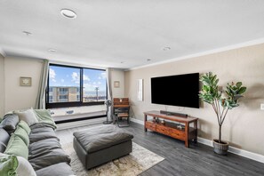 A modern living room with a sofa, ottoman, TV, and a potted plant.