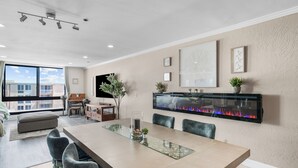 Un espace de repas moderne avec une table à plateau en verre, des chaises rembourrées, une cheminée et une vue sur la ville.