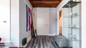 Un pasillo con techo de madera, un aparador de vidrio con estantes y una puerta al final.