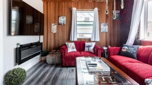 Una sala de estar acogedora con un sofá rojo, una mesa de centro y un televisor de pantalla plana montado en la pared.