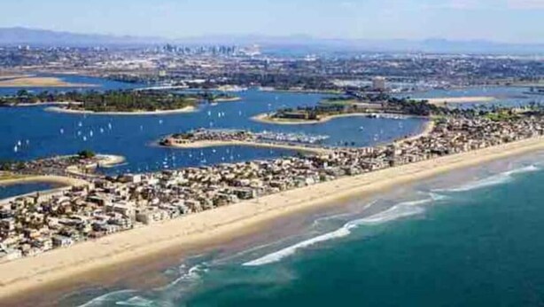 Un paisaje urbano costero con playa, puerto deportivo y zona residencial.