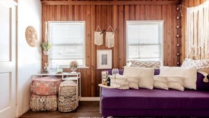 A cozy room with a purple sofa, wooden walls, and a small table with a globe and a plant. - Tuluminati:BohoChic Condo Steps from Ocean and Bay (San Diego)