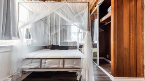 A bedroom with a canopy bed, wooden flooring, and a closet with wooden paneling. - Luxe Thai-Inspired Condo Steps to Beach w/ Parking (San Diego)