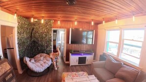 A cozy living room with a wooden ceiling, a bean bag chair, a television, and a large window. - Luxe Thai-Inspired Condo Steps to Beach w/ Parking (San Diego)