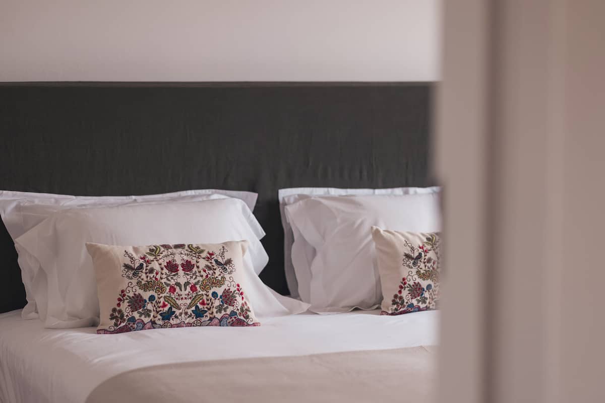 A neatly made bed with white linens and two decorative pillows with floral patterns.
