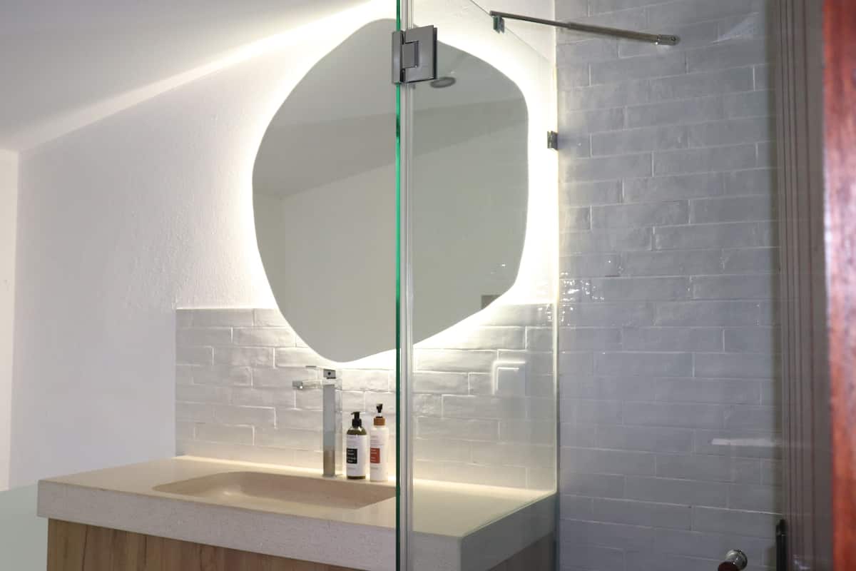 A bathroom with a round mirror, a sink, and toiletries on the counter.