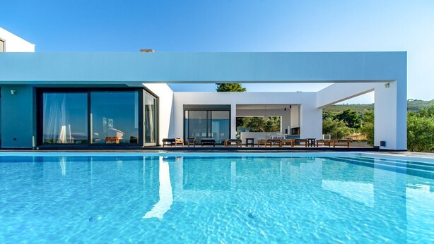 Ein moderner Pool mit klarem, blauem Wasser, ein überdachter Sitzbereich mit Tischen und Stühlen sowie ein großer Glastür-Eingang.