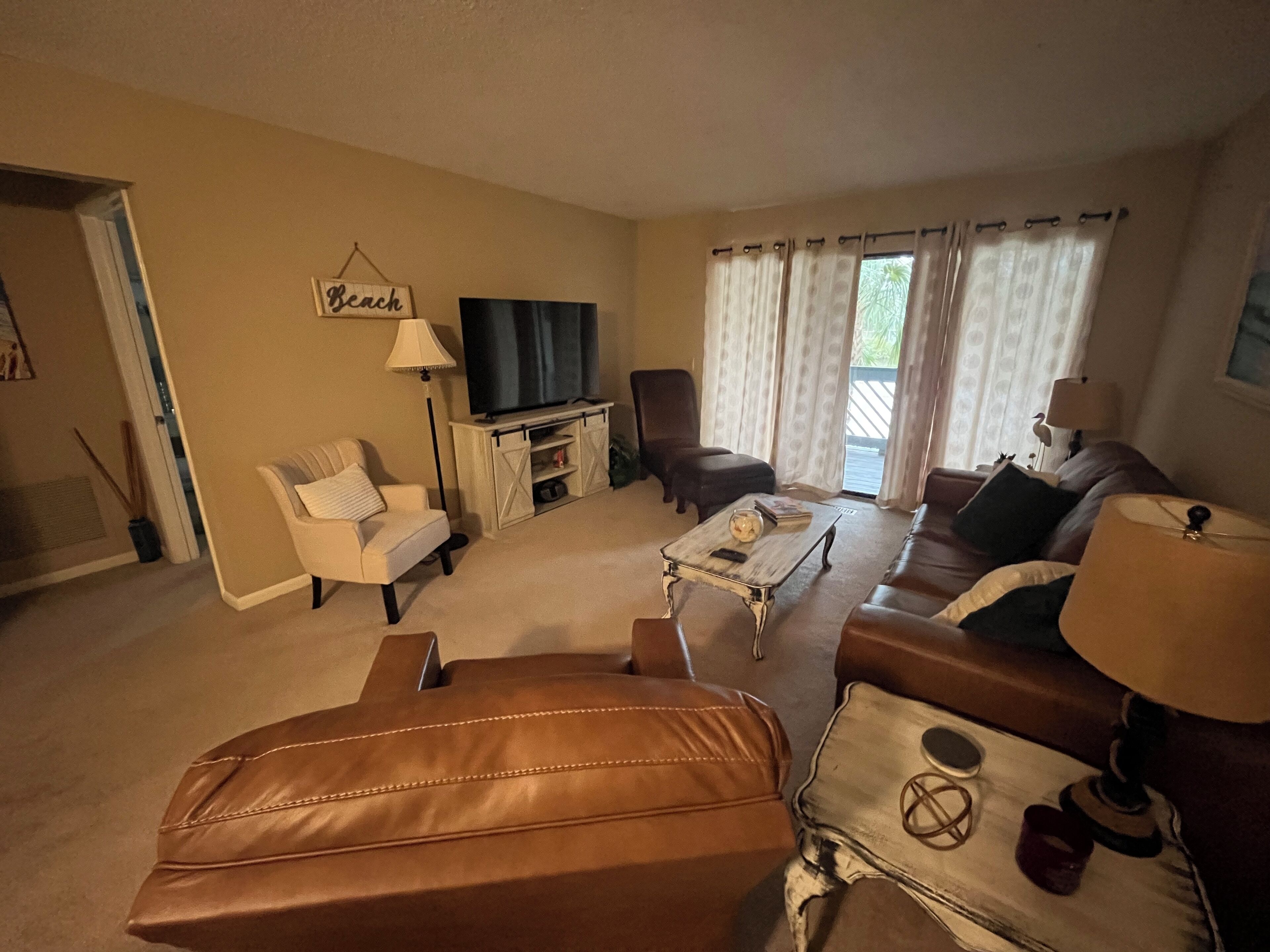 A living room with a sofa, armchairs, a coffee table, a TV, and a sign that reads "Beach".