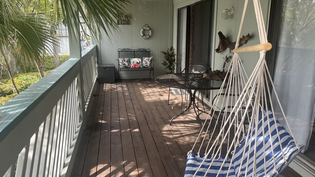 Ett trädäck med en hängstol, en bänk med kuddar och ett litet bord.