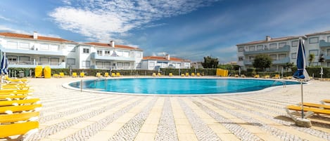 A swimming pool with yellow lounge chairs and a tiled deck.