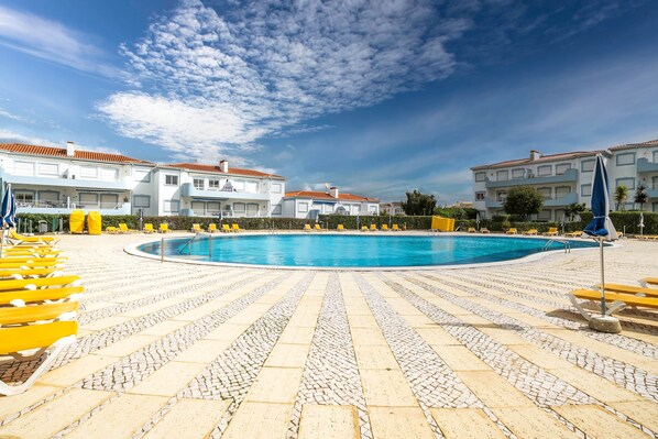 A swimming pool with yellow lounge chairs and a tiled deck.