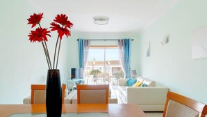 A living room with a dining table, chairs, a sofa, and a view of a balcony with a railing. - Lovely 2 Bedroom Apt, Oasis Parque, Alvor (Portimão)